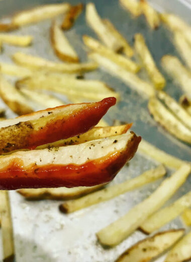 A pan with french fries on it with a few fries with ketchup on them.