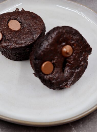 Two chocolate with chocolate chips muffins sitting on a grey plate.
