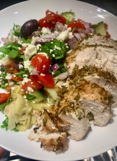 A white plate with sliced herb chicken on it and a beautifully colored salad.