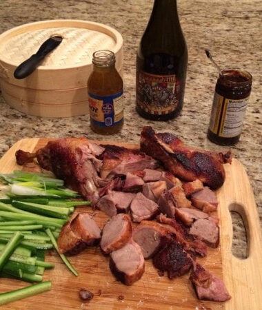 Delicious cutting board full of sliced Peking duck and vegetables with assorted sauces and wine for steamed buns with Peking Duck.