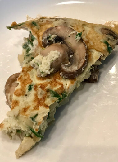 A white plate with a slice of mushroom, spinach and onion frittata on top.