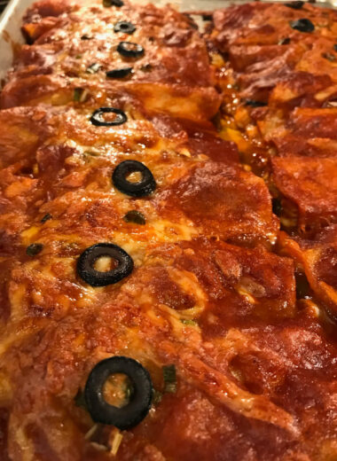 A pan of enchiladas with melted cheese and a black olive slice on top of each one.
