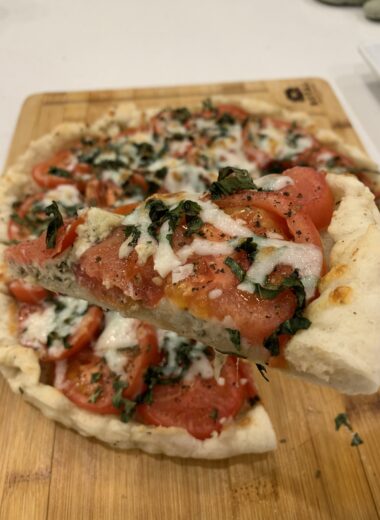 A pizza slice being held above a pizza sitting on a wooden cutting board.