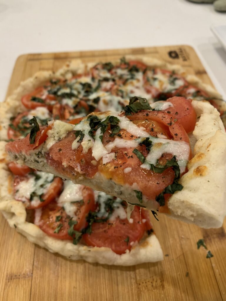 A pizza slice being held above a pizza sitting on a wooden cutting board.