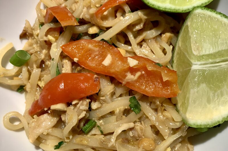 A bowl with delicious pad thai inside of it with lime wedges