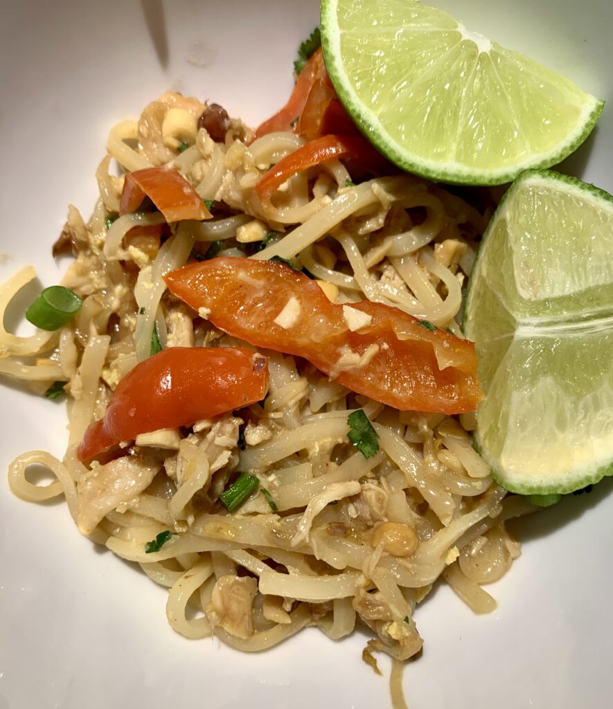 A bowl with delicious pad thai inside of it with lime wedges