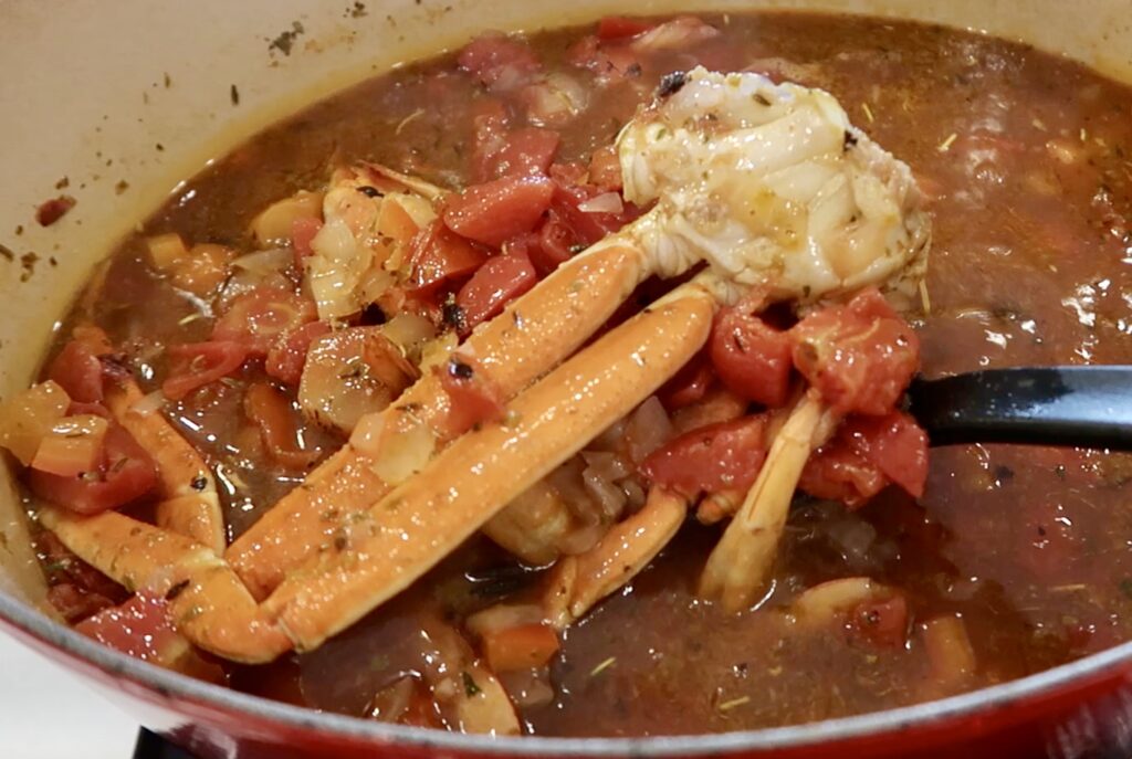 A big pot full of broth and seafood with crab legs