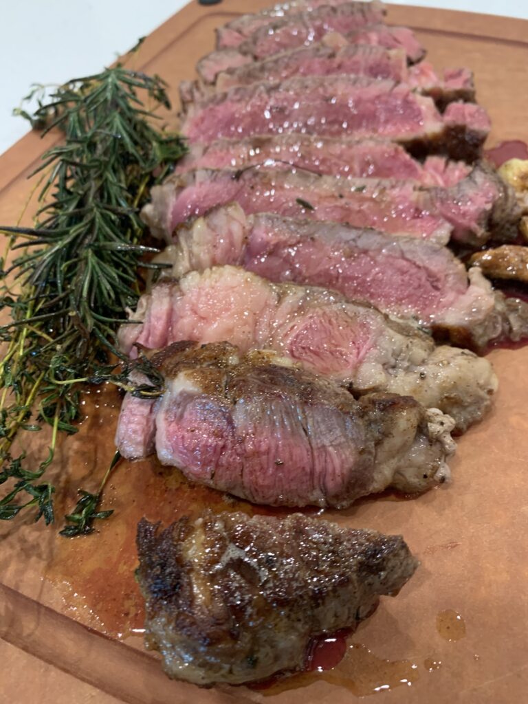 A cutting board with rare steat cut into pieces on it.