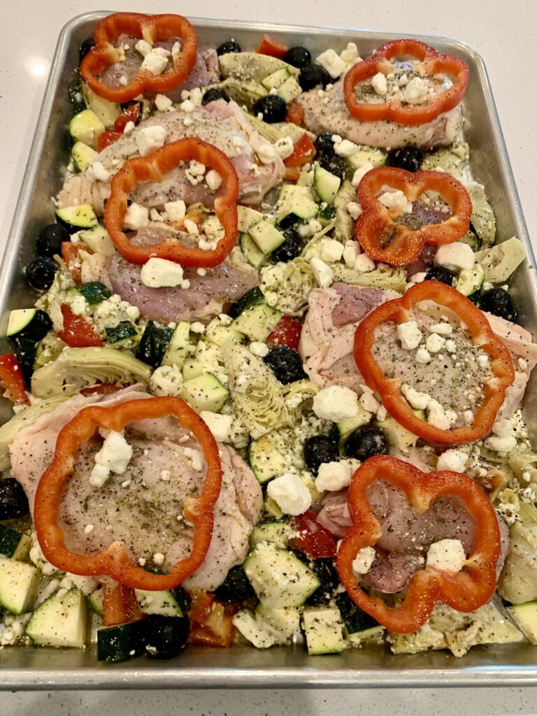 A sheet pan with chicken peppers, onions, olives and feta on it.
