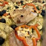 A sheet pan with baked chicken, onions, olives and feta on it.