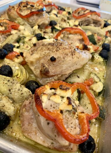 A sheet pan with baked chicken, onions, olives and feta on it.