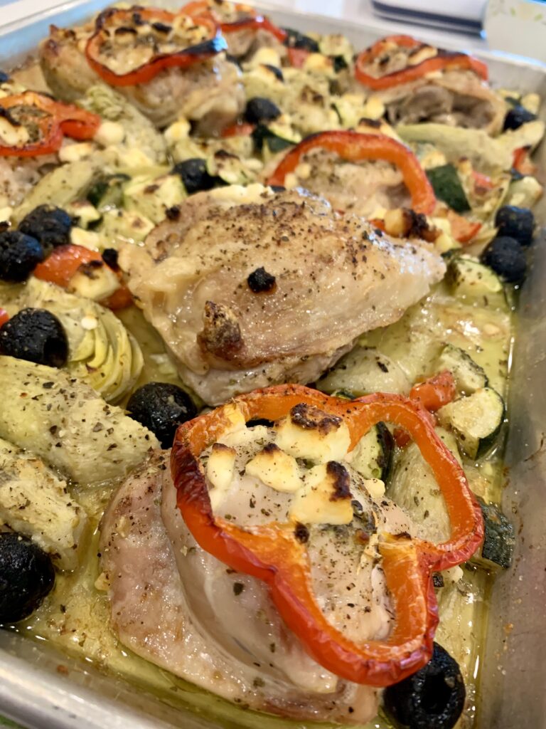 A sheet pan with baked chicken, onions, olives and feta on it.