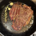 A cast iron pan with a perfectly seared steak in it with rosemary and garlic