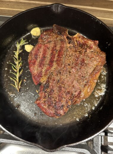 A cast iron pan with a perfectly seared steak in it with rosemary and garlic