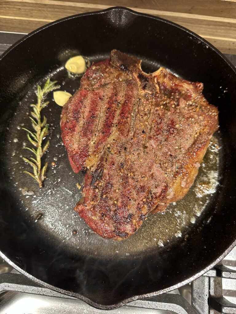 A cast iron pan with a perfectly seared steak in it with rosemary and garlic