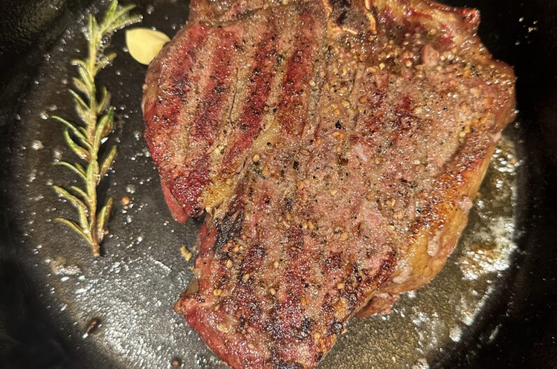 A cast iron pan with a perfectly seared steak in it with rosemary and garlic